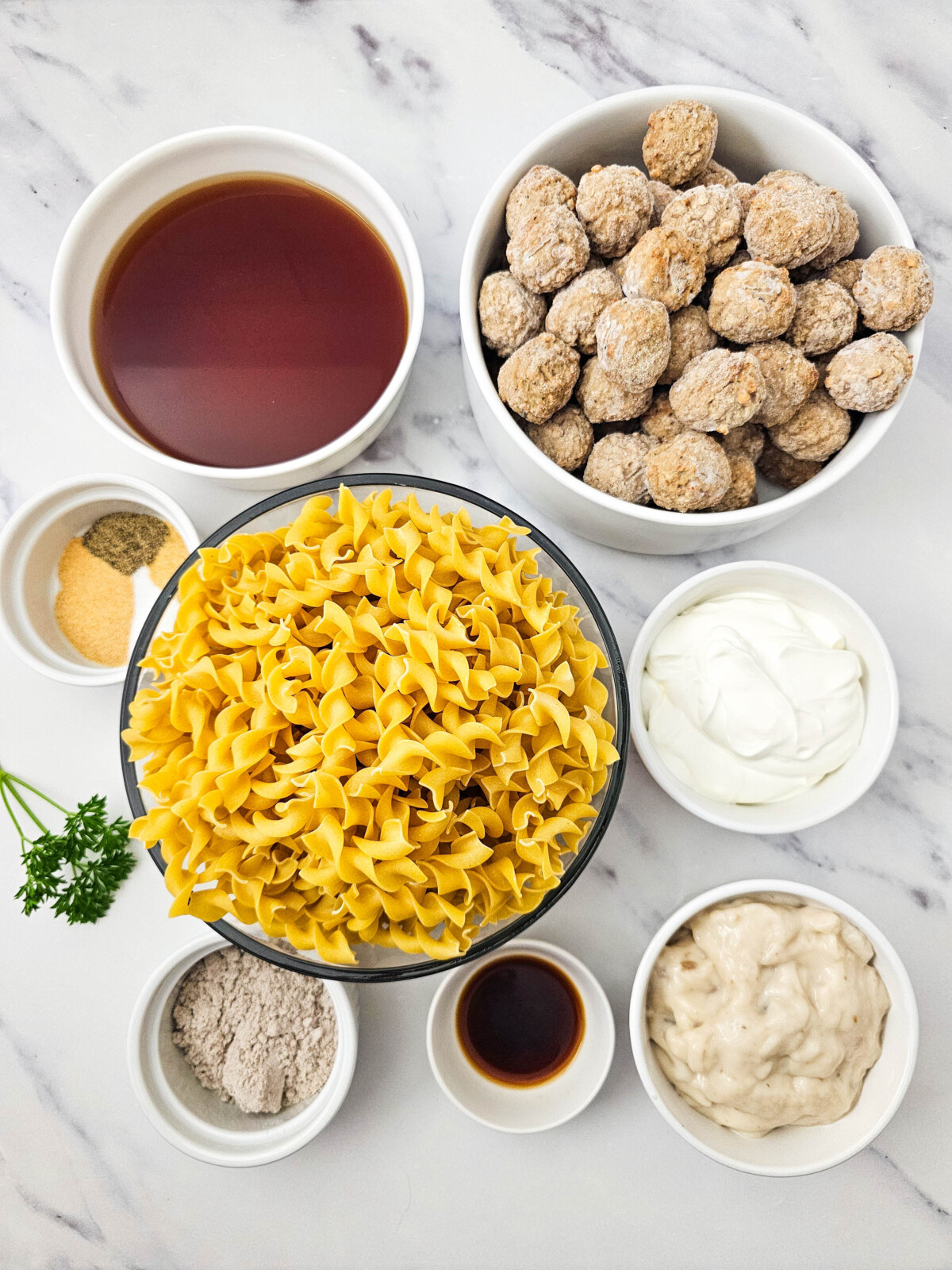 Swedish meatballs ingredients laid out flat including meatballs, pasta, sour cream, mayo, and seasonings on marble background
