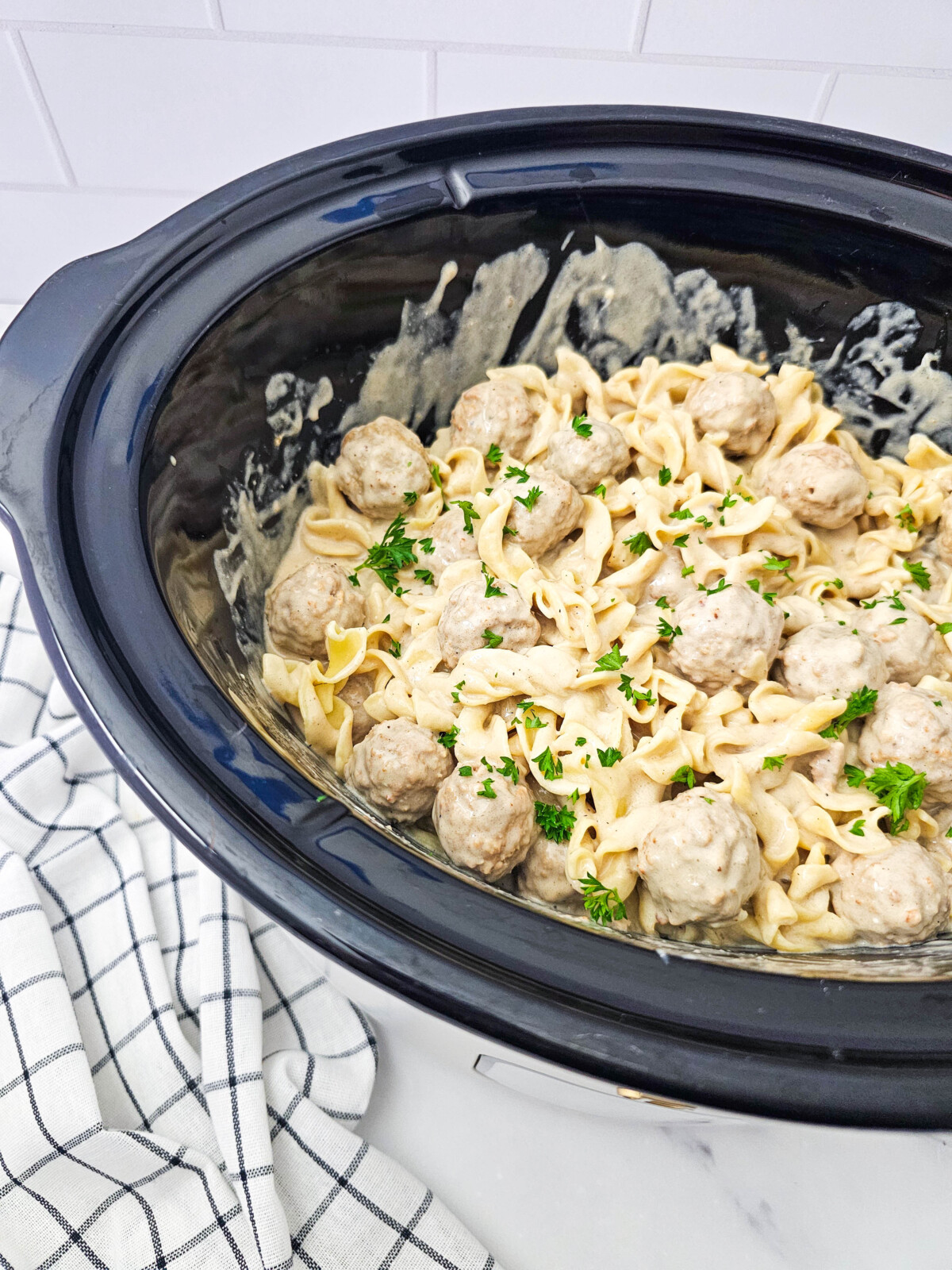 Crockpot Swedish meatballs with egg noodles in creamy sauce garnished with parsley