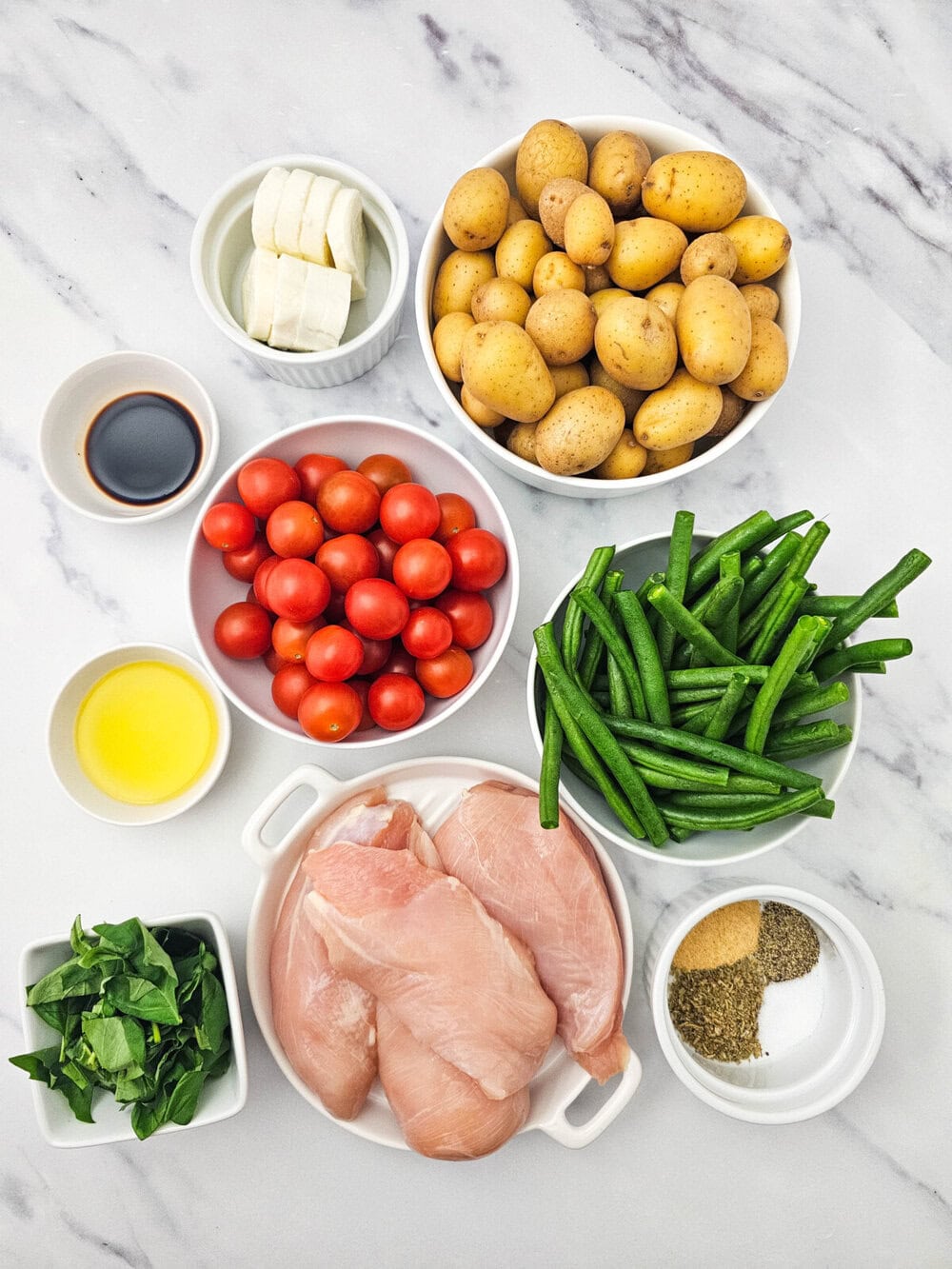 Sheet Pan Chicken Caprese ingredients arranged overhead - raw chicken, potatoes, tomatoes, green beans, mozzarella, spinach, and seasonings