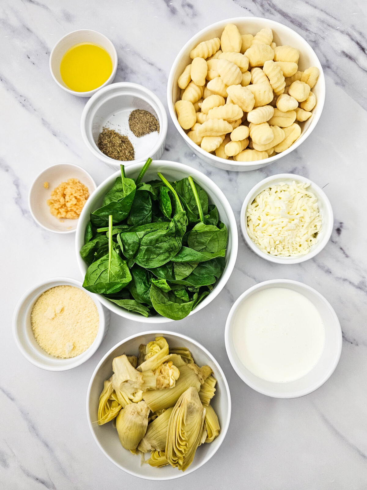 Skillet Spinach Artichoke Gnocchi ingredients laid out in bowls from above including gnocchi, spinach, artichokes, mozzarella, parmesan, cream, and seasonings