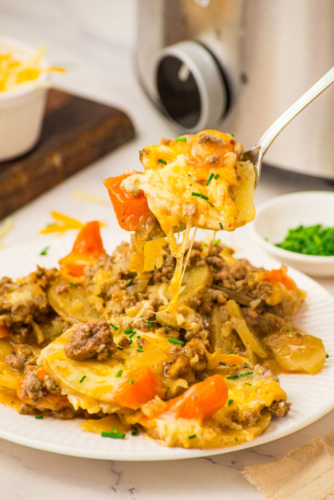 Slow cooker layered beef and potatoes with melted cheese and peppers on white plate