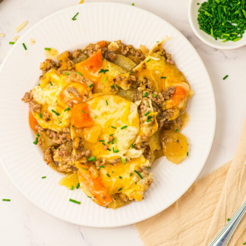 Slow cooker layered beef and potatoes with melted cheese and chives on white plate
