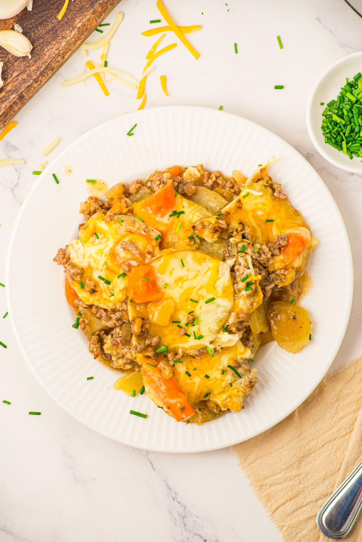 Slow cooker layered beef and potatoes casserole with melted cheese and peppers on white plate