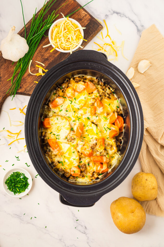 Slow cooker beef and potato casserole with cheese topping, overhead view with prepared ingredients